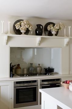 a kitchen with white cabinets and black plates on the shelf above the stove top oven