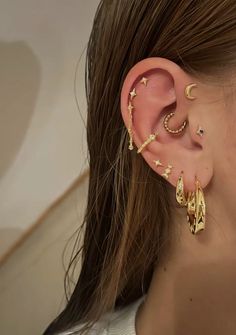 a woman wearing gold ear cuffs with stars and moon designs on the side of her ear