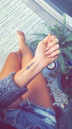 a person with a tattoo on their arm sitting next to a potted fern plant