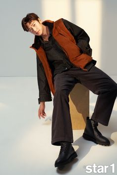 a young man sitting on top of a box wearing black pants and an orange shirt