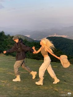 a man and woman walking on top of a lush green hillside