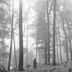 black and white photograph of two people walking through the woods on a foggy day