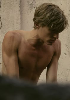 a shirtless young man leaning against a wall