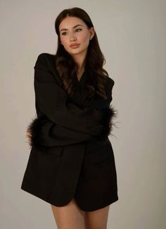 a woman wearing a black suit and fur collar posing for the camera with her arms crossed