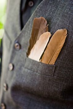 a man in a suit with two feathers sticking out of his pocket and another feather stuck to the back of his jacket