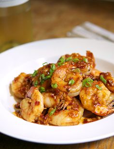 a white plate topped with shrimp covered in sauce and garnished with green onions