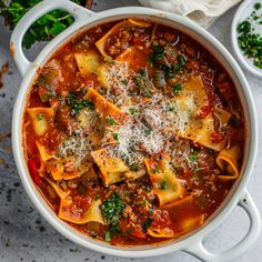 a white pot filled with pasta and meat sauce next to parmesan cheese on top