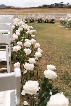 rows of white chairs lined up in the grass with flowers on each chair and one row of them