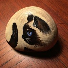 a painted rock with a black and white cat's face on it sitting on a wooden table