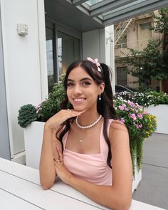 a woman sitting at a table with her hand on her chin and wearing a pearl necklace