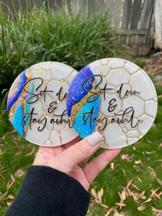 someone holding two marble coasters with words on them