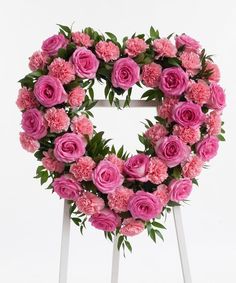 pink flowers arranged in the shape of a heart on a white stand with green leaves