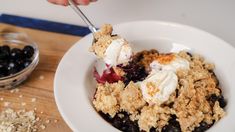 a bowl filled with blueberries and ice cream on top of a wooden cutting board