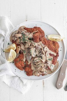 a white plate topped with fried chicken covered in mushroom gravy and lemon wedges