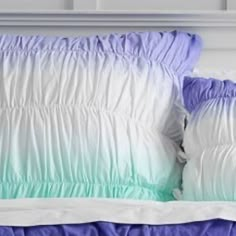 two pillows sitting on top of a bed next to a white headboard with blue and green ruffles