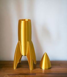 a gold rocket ship vase sitting on top of a wooden table next to a golden cone