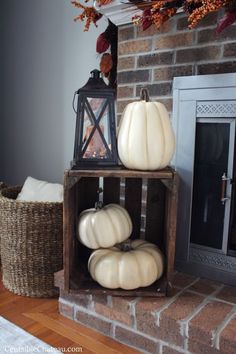 three white pumpkins sitting on top of a wooden crate in front of a fireplace