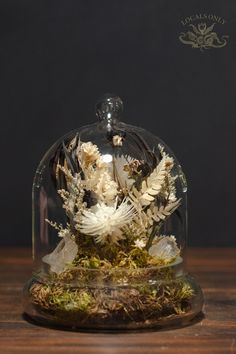 a glass dome with moss and flowers inside on a wooden table in front of a black wall