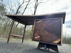 an upside down wooden table sitting on the side of a road next to a forest