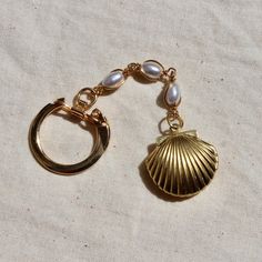 a gold charm with a shell and pearls hanging from it's side on a white cloth