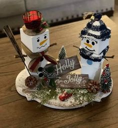 two snowmen sitting on top of a wooden table next to a sign that says holly jolly