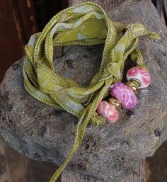 two pink and green beads sitting on top of a wooden post next to a yellow scarf