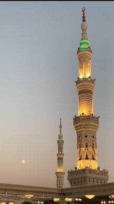 two tall towers lit up at night with the moon in the background