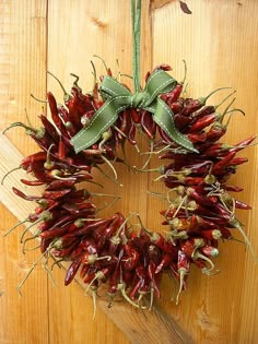 a wreath made out of dried red peppers hanging on a wooden wall with a green bow