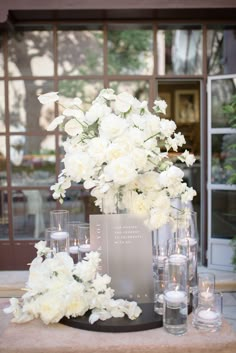 white flowers and candles are arranged on a table in front of a glass building with windows