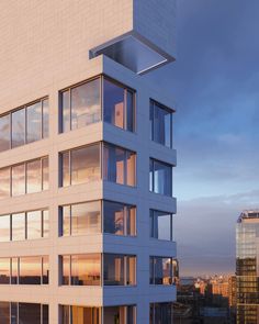 a tall white building with lots of windows next to a cityscape at sunset