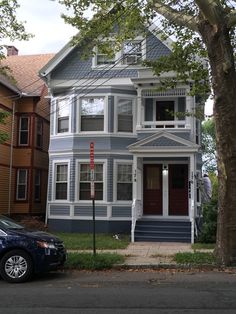 a car parked in front of a two story house with blue siding and white trim