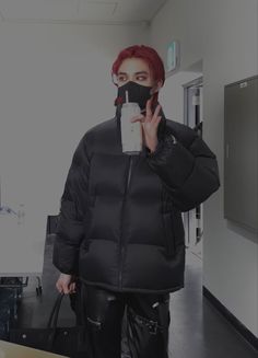 a woman with red hair wearing a black puffer jacket and holding a cell phone up to her face