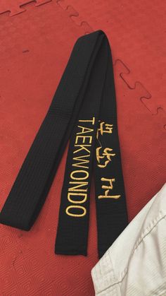 two black karate belts laying on top of a red floor next to a pair of white pants