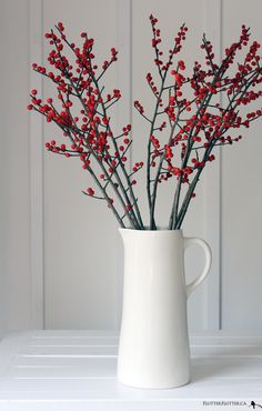 a white vase filled with red berries on top of a table