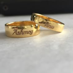 two gold wedding rings with the words ashney and you engraved on them sitting on a table