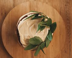 a cake with white frosting and green leaves on a wooden platter, top view from above