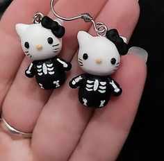 two hello kitty skeleton earrings are shown in the palm of someone's hand,