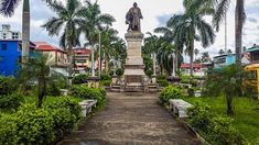 a statue in the middle of a garden with trees and bushes around it, surrounded by buildings