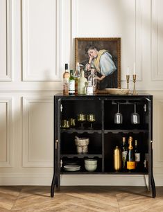 a black cabinet with bottles and glasses on it next to a painting in a room