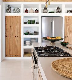 a kitchen with wooden cabinets and white counter tops, an island in the middle has plates on it