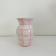 a pink and white vase sitting on top of a table next to a white wall