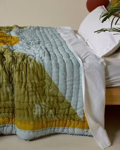 a bed with a green and yellow quilt on it next to a plant in a vase