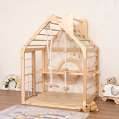 a doll house made out of wood on the floor next to a teddy bear and other toys