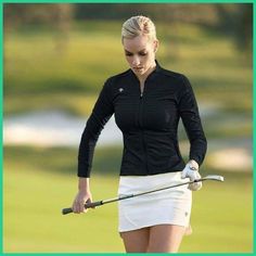 a woman holding a golf club on top of a green field