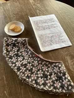 a crocheted table runner next to a bowl of cookies on a wooden table