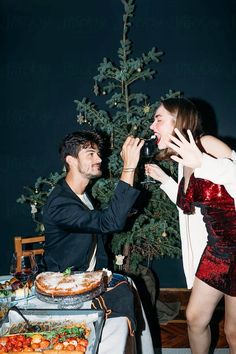 a man feeding a woman cake at a table with christmas tree in the back ground