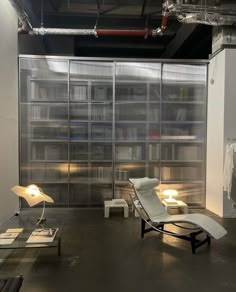 an empty room with chairs and lamps on the floor in front of glass walls that have bookshelves behind them