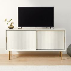 a flat screen tv sitting on top of a white cabinet next to a vase with flowers