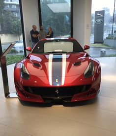 a red sports car is on display in a showroom with people looking at it