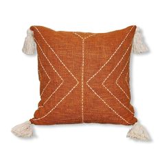 an orange and white pillow with tassels on the edges, sitting on a white surface